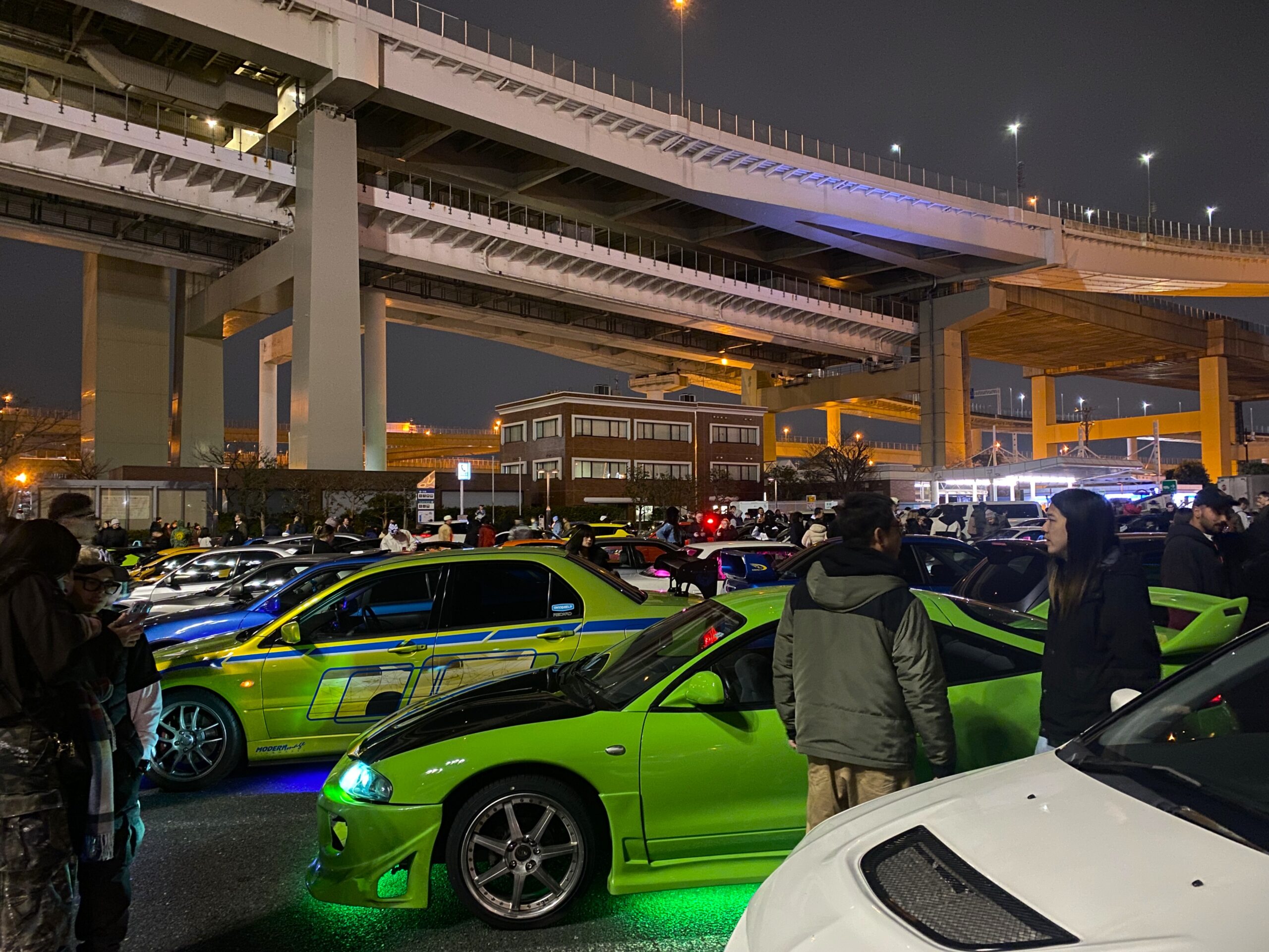 Tuned JDM sports car with bright green neon underglow parked safely at the Daikoku PA nighttime car meet.
